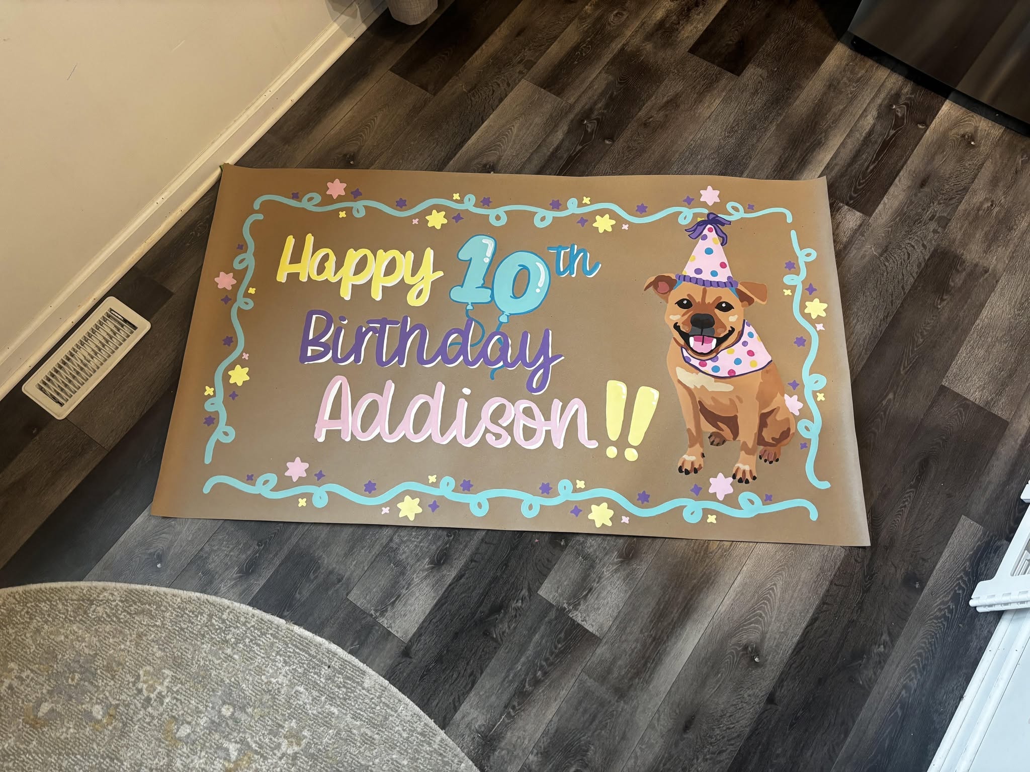 Hand-painted 'Happy 10th Birthday Addison' banner on kraft paper with a painted portrait of the birthday dog in a party hat